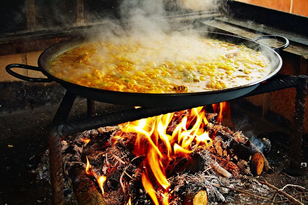 Traditional Valencian paella cooking over an open flame in a wide shallow pan — 1