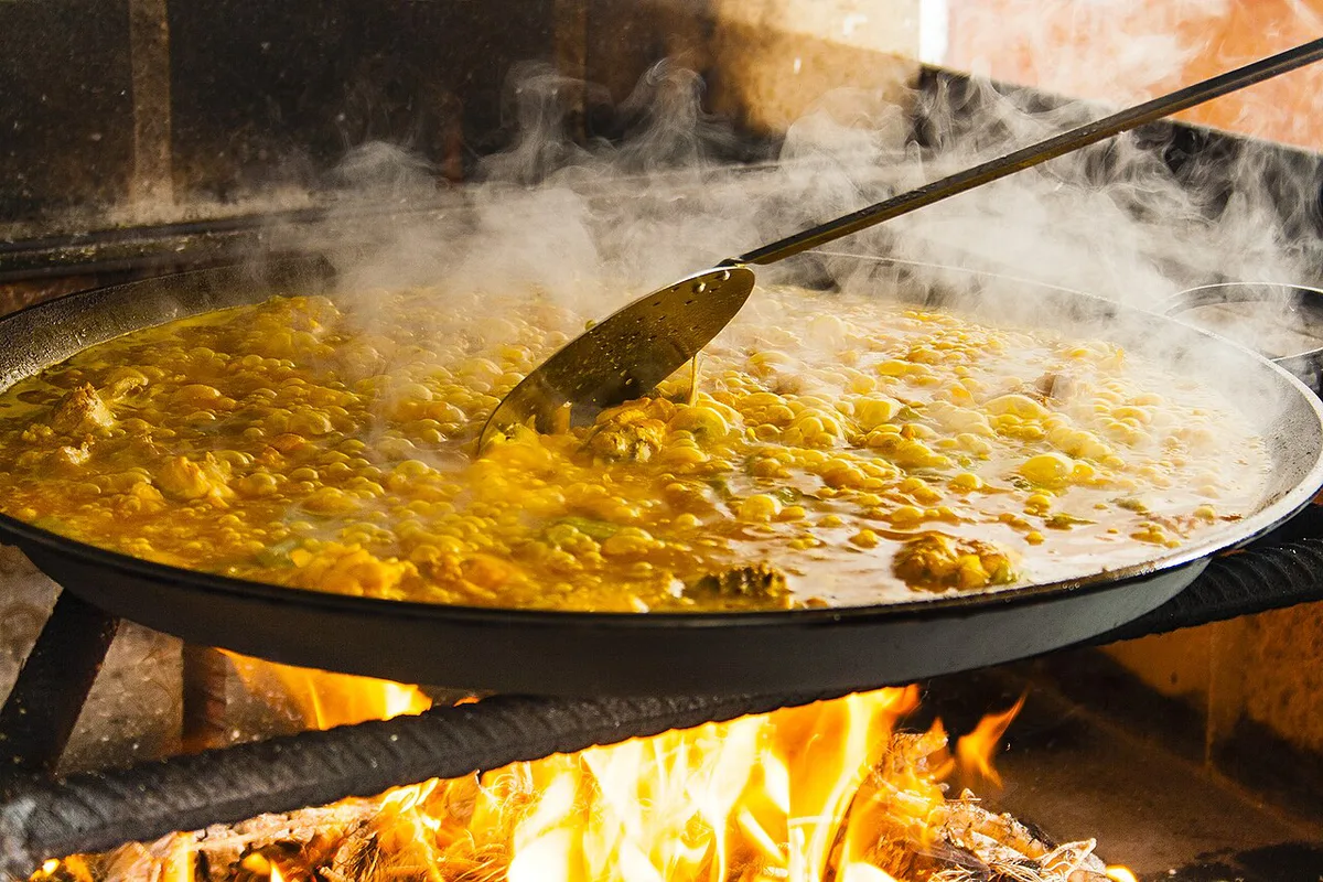 Traditional Valencian paella cooking over an open flame in a wide shallow pan — 2