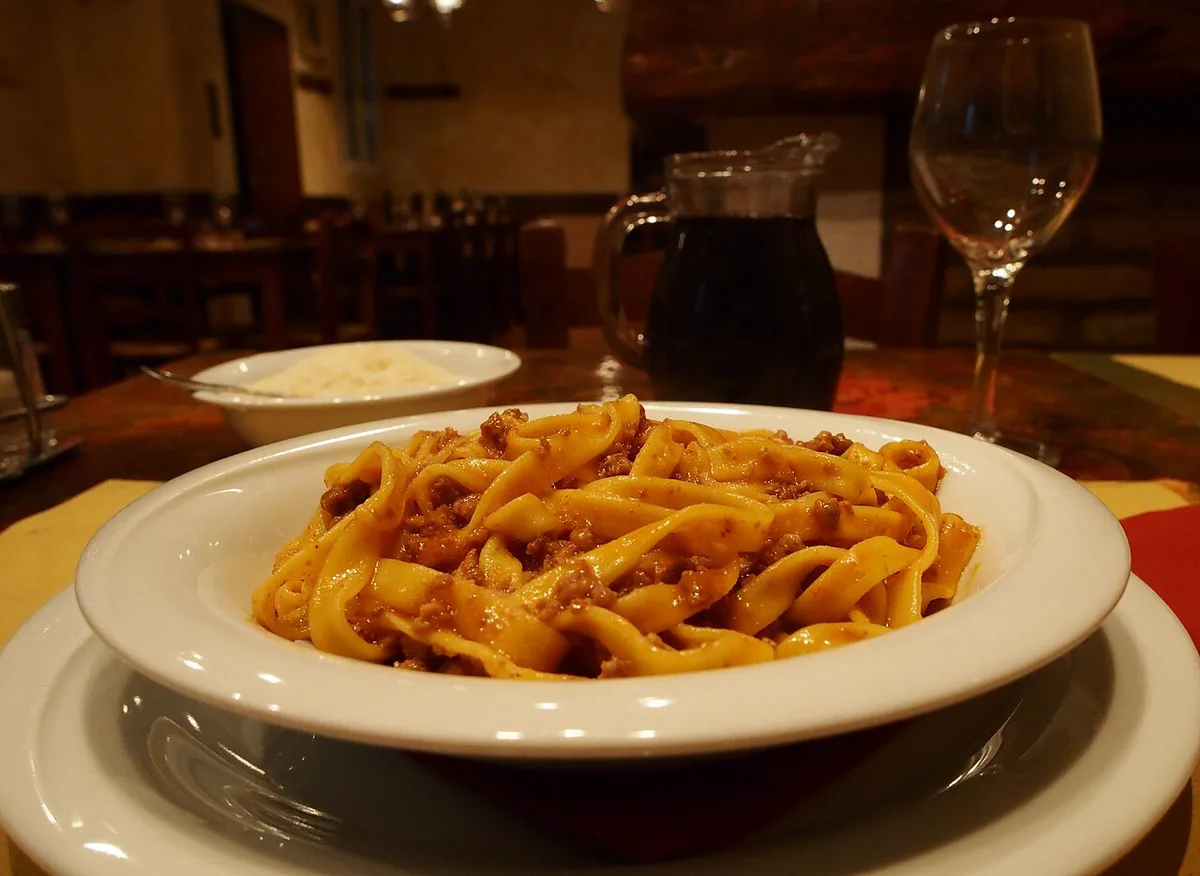 Fresh tagliatelle al ragù alongside sliced mortadella and Parmigiano on a wooden board in Bologna — 1