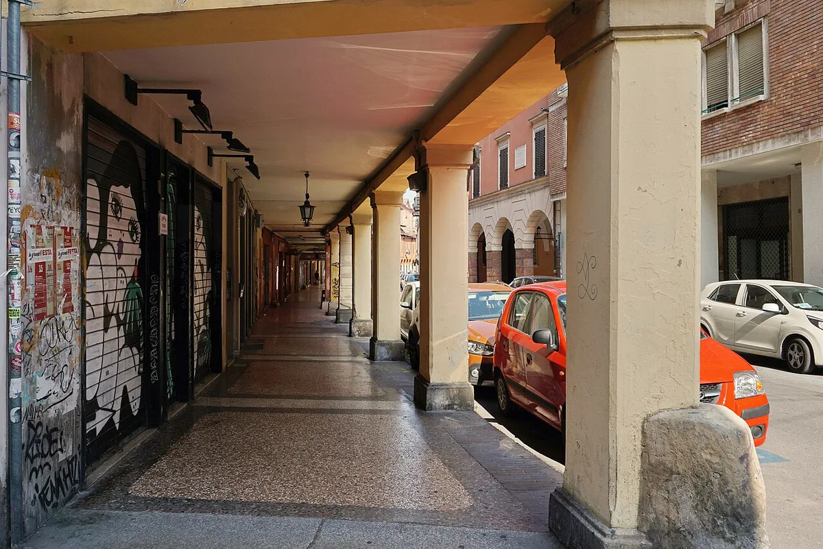 Porticoed street in Bologna's historic center with terracotta buildings under a covered walkway — 1