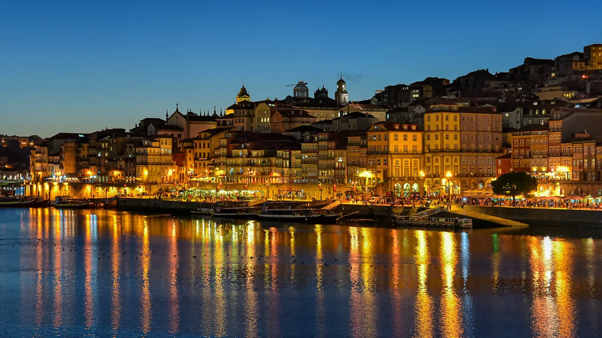 Iconic Dom Luís I Bridge spanning the Douro River in Porto, with colorful Ribeira buildings and traditional boats below